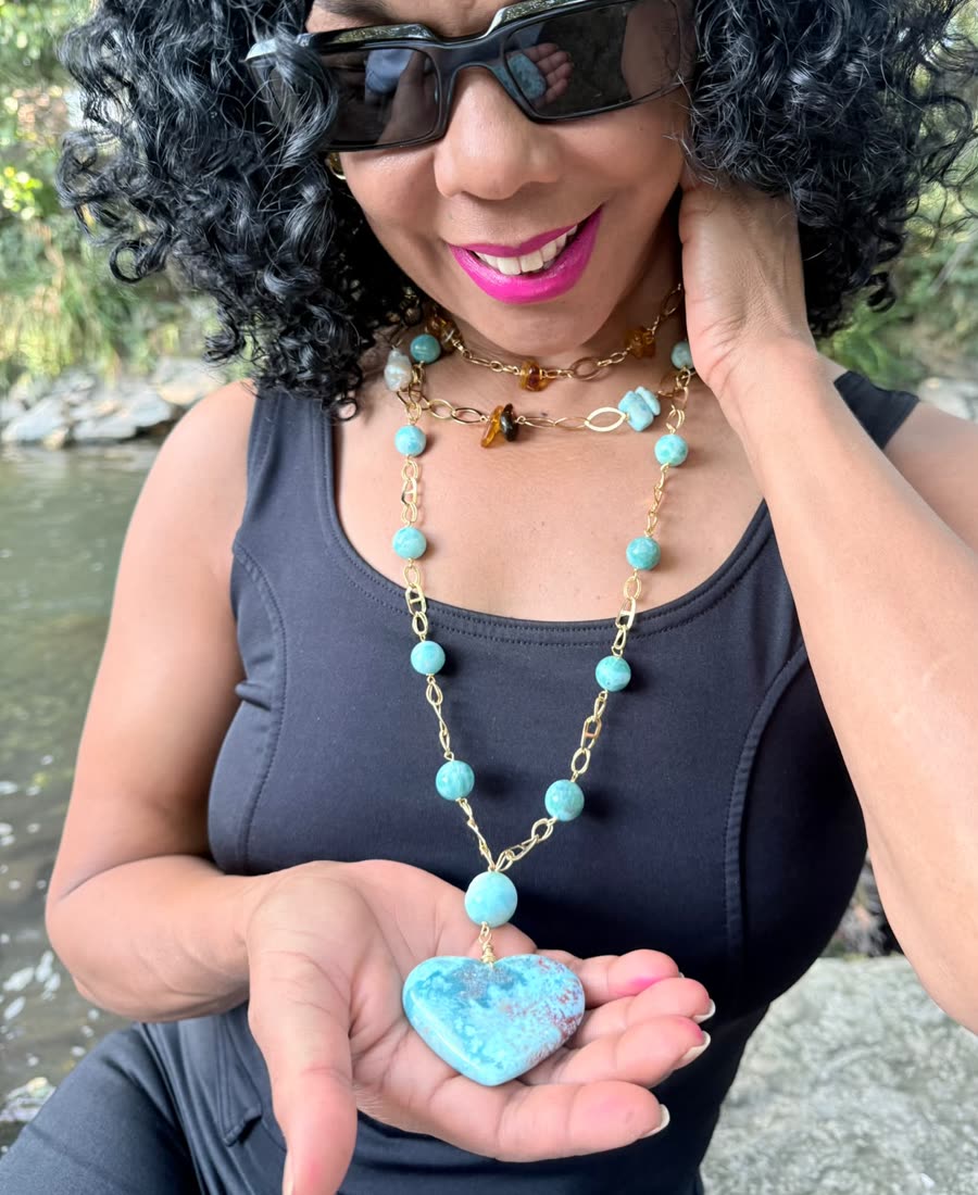 Woman wearing a larimar necklace, holding the heart-shaped pendant in her hand