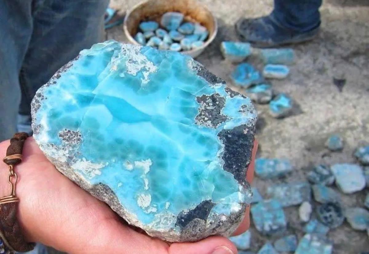 Large piece of raw larimar held in a hand, with smaller larimar pieces nearby